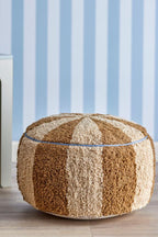 Charoline Pouf Brown – Bloomingville MINI : pouf devant un mur habillé de papier peint à rayures bleues.