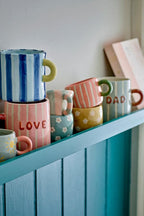 Cherish Mug Blue – Handbemalte Keramiktasse mit Dad – Bloomingville: verschiedene bunte Tassen auf einem Schrank.