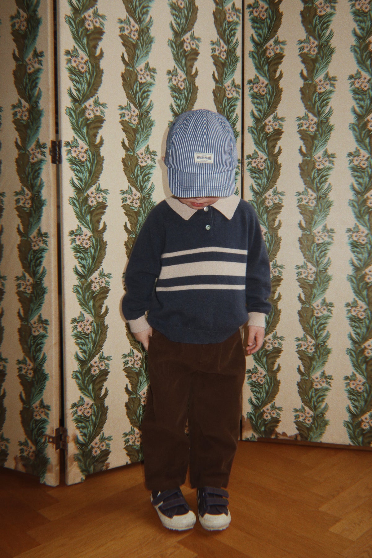 Wollen polo Basi – Dark Blue Stripe – Konges Sløjd: kind met donkerblauwe gestreepte polo, bruine broek en blauwe muts.