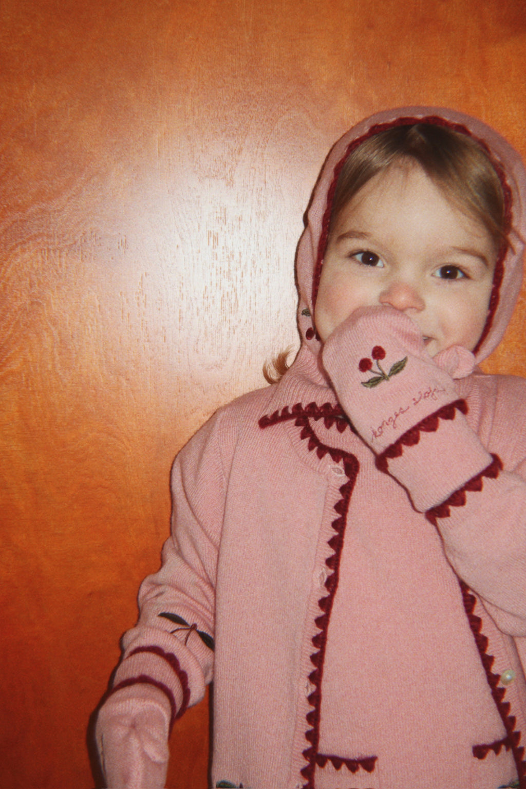 Wollen balaclava Collette – Pale Blush – Konges Sløjd: kind met roze kersenvest houdt de mouw bij het gezicht.