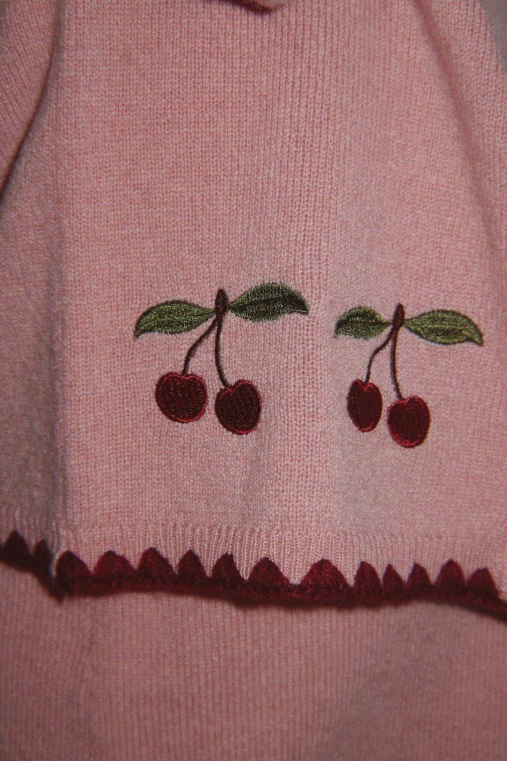 Wollen vest Collette – Pale Blush – Konges Sløjd: detail van de geborduurde kersen en onderrand van het roze vest.